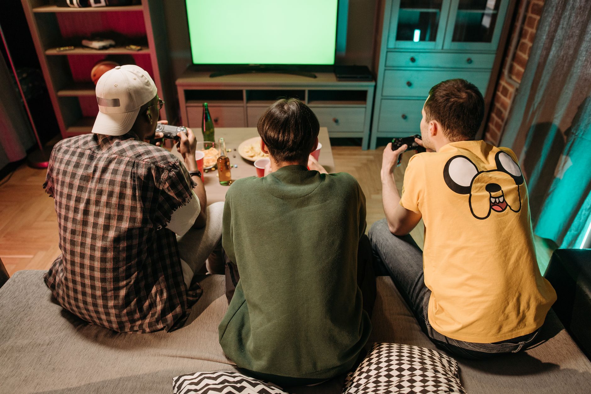 Three young men enjoying a home gaming session together, playing video games in a cozy indoors setting. — Bookmakers Uden Dan