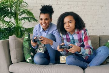 Two teenagers playing video games together on a comfortable couch, surrounded by indoor plants. — How MPO007 Login Gives Play