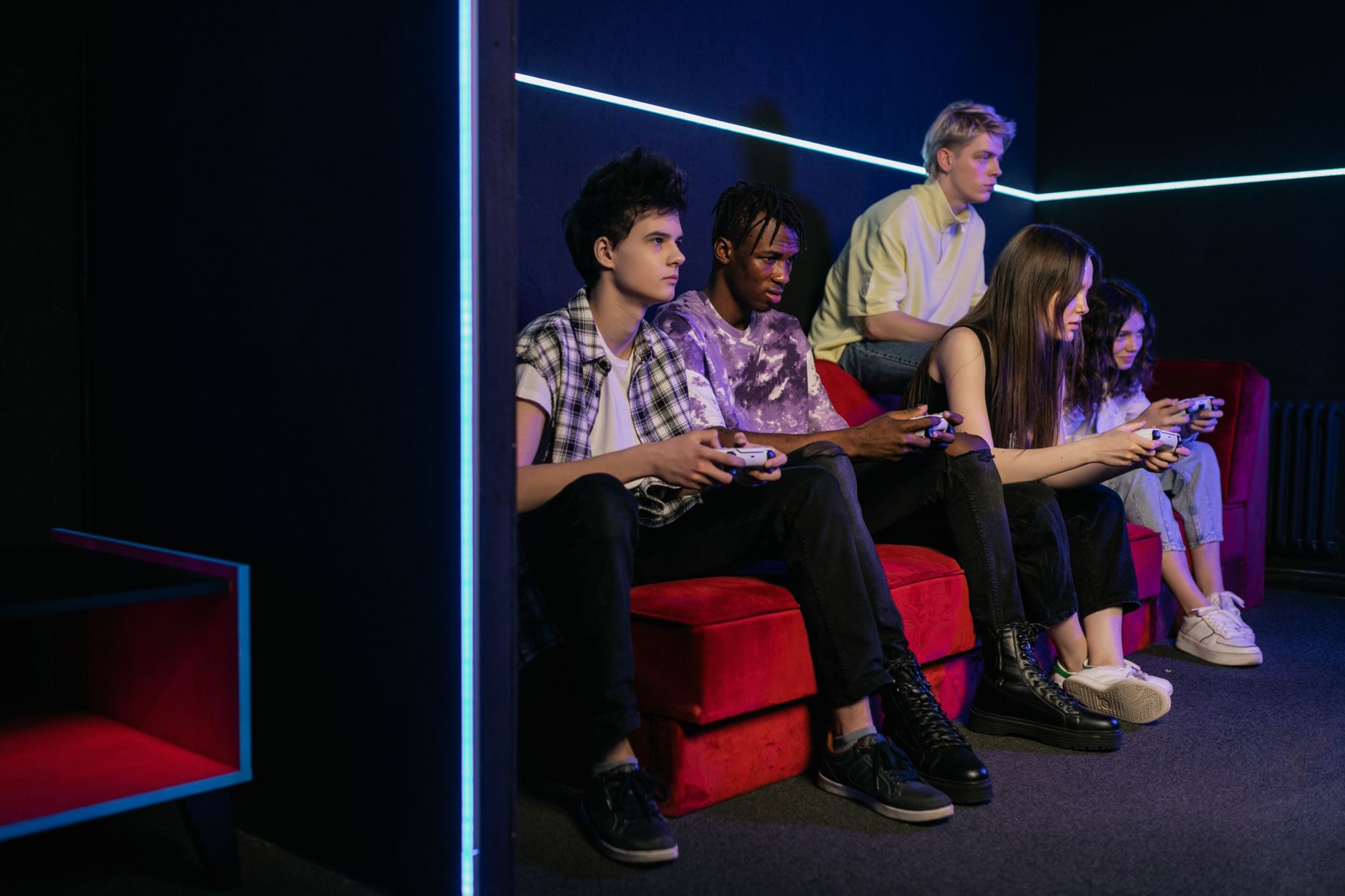 Teenagers enjoying video games together on a vibrant red couch in a modern gaming room. —