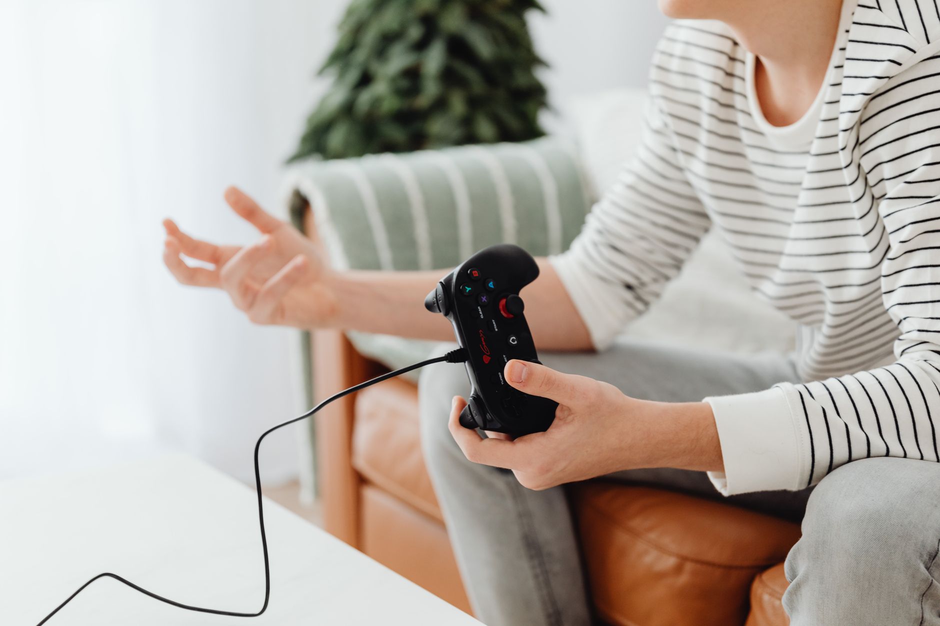 Close-up of a person playing video games at home with a wired controller on a couch. — title