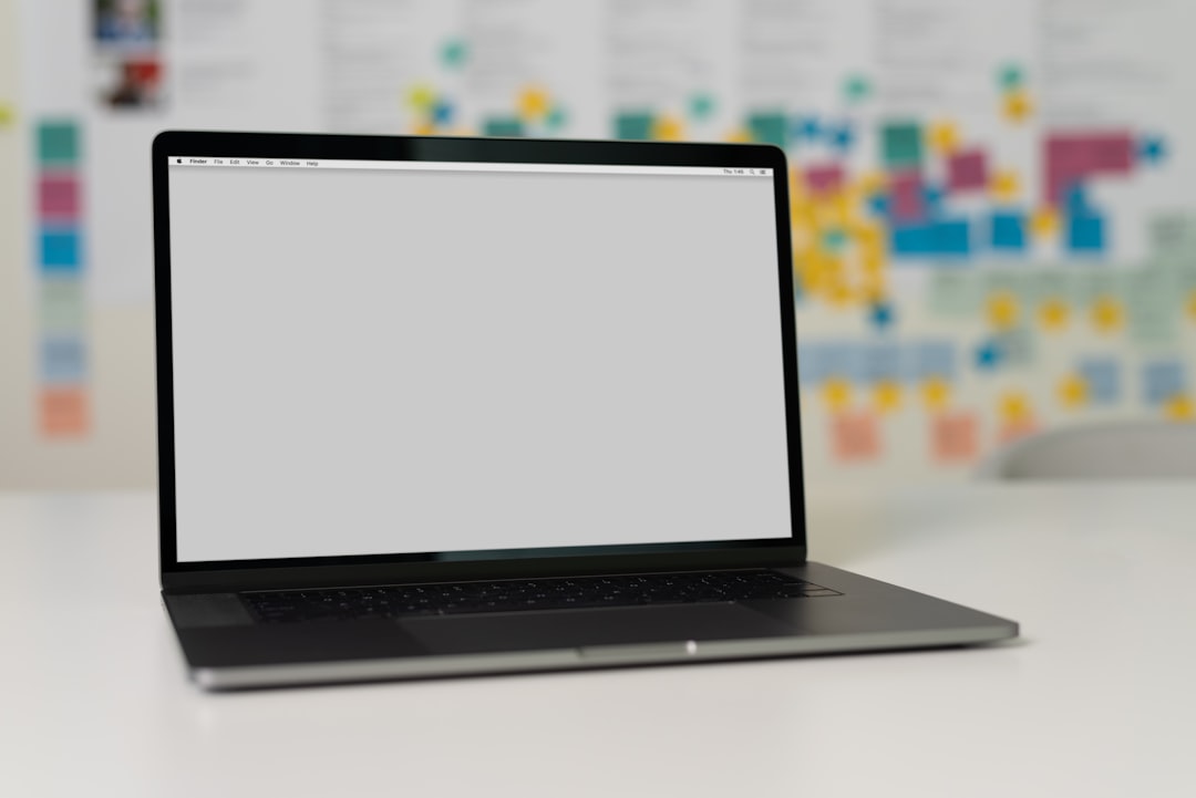 a laptop on a table with a blank screen and colorful sticky notes in the background
